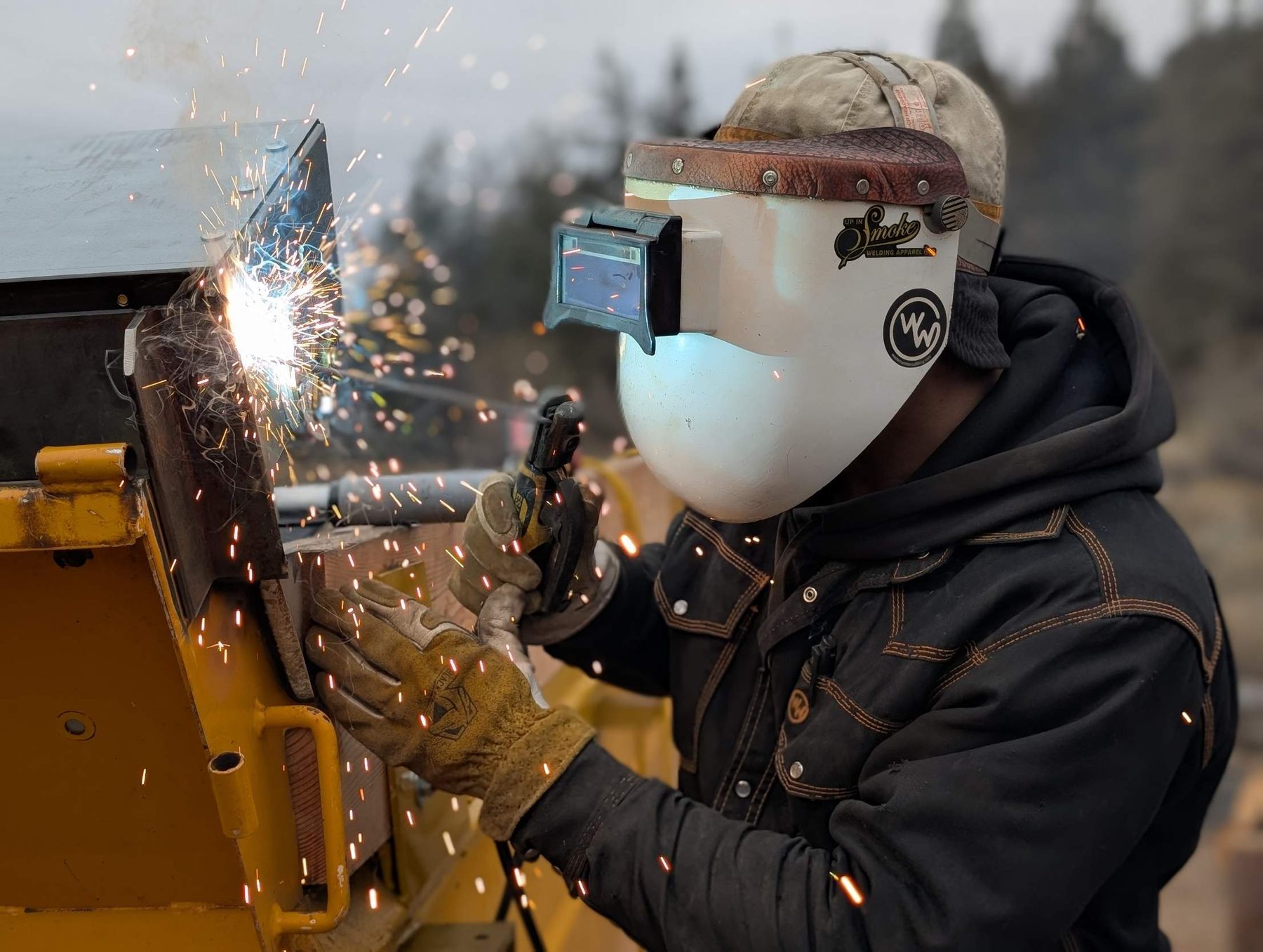 Welding a repair on yellow heavy equipment in the field, sparks flying