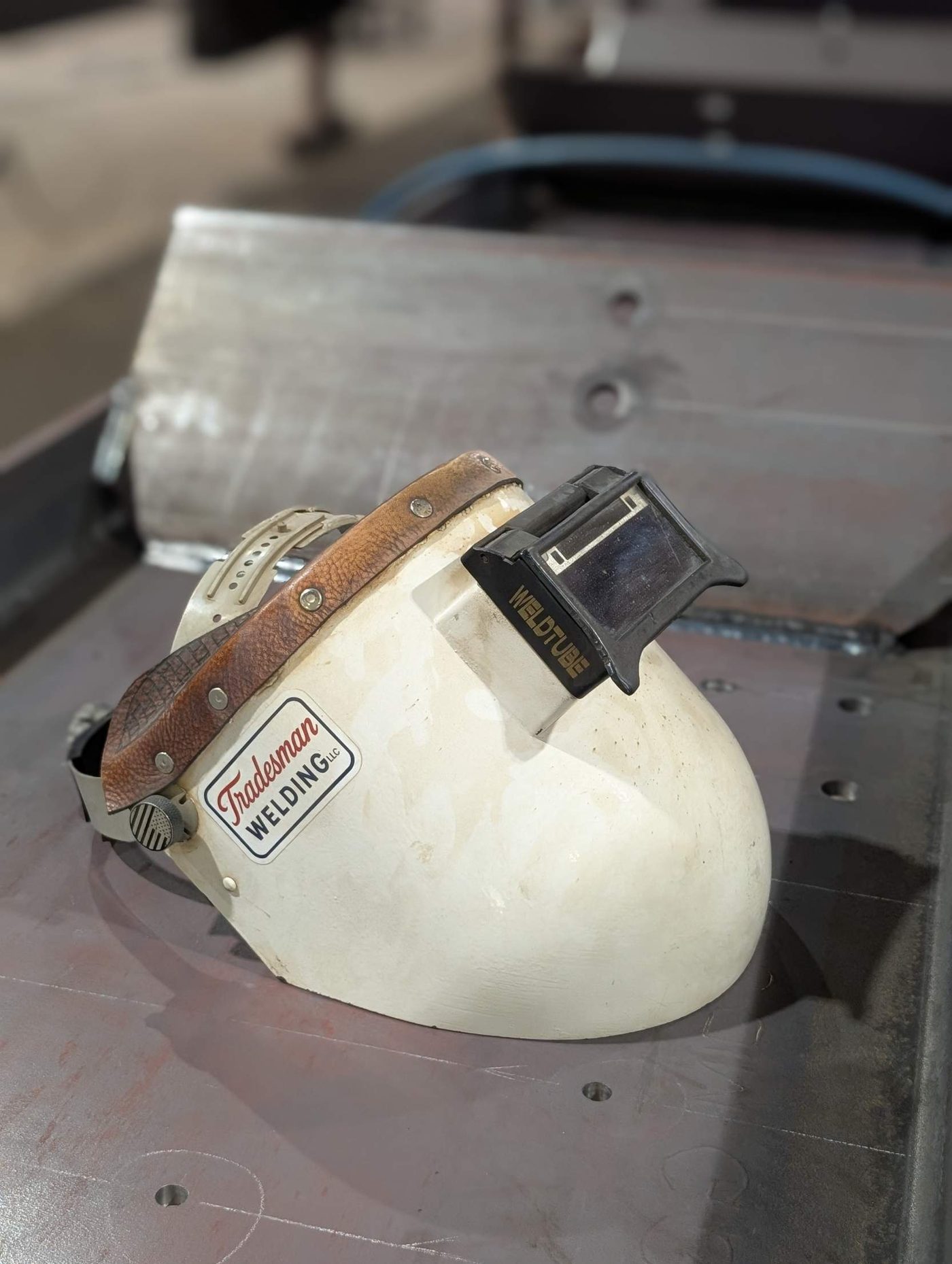 Pancake welding hood with a Tradesman Welding sticker, resting on a steel plate