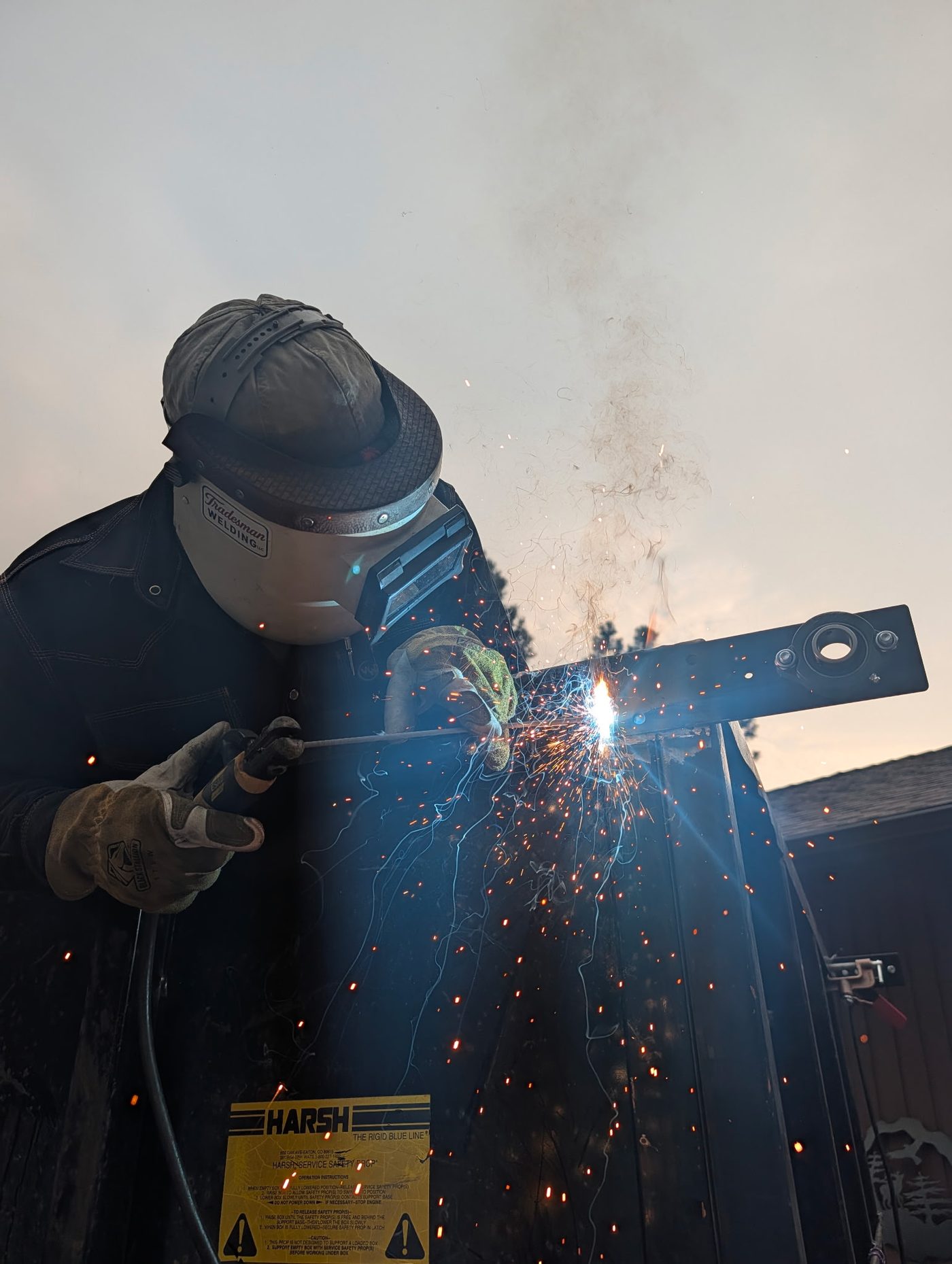 Welding a steel bracket outdoors in a Tradesman Welding hood, sparks flying